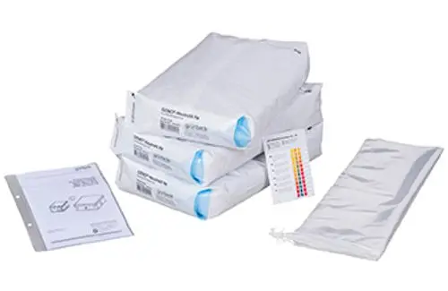 Wartungsset von Grünbeck bestehend aus mehreren weißen, in Folie verpackten Komponenten und einer Anleitung in einem Ordner, neben einer transparenten Tasche.